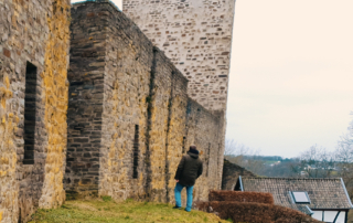 Eine Person blickt an einer Stadtmauer mit Turm empor